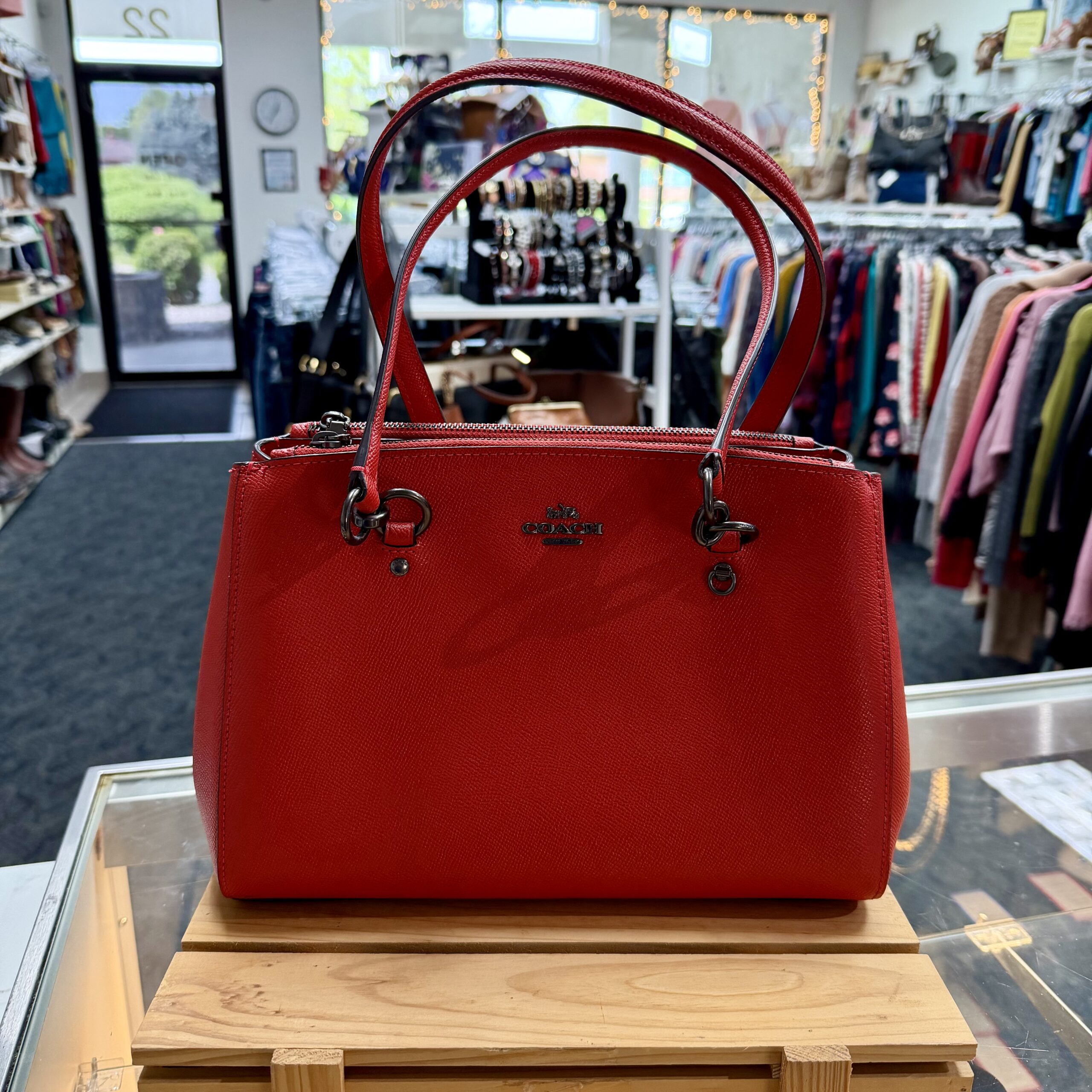 Authentic Coach purse in red leather satchel handbag with black hardware, double top handles, and zip-top closure displayed in a women's consignment boutique.