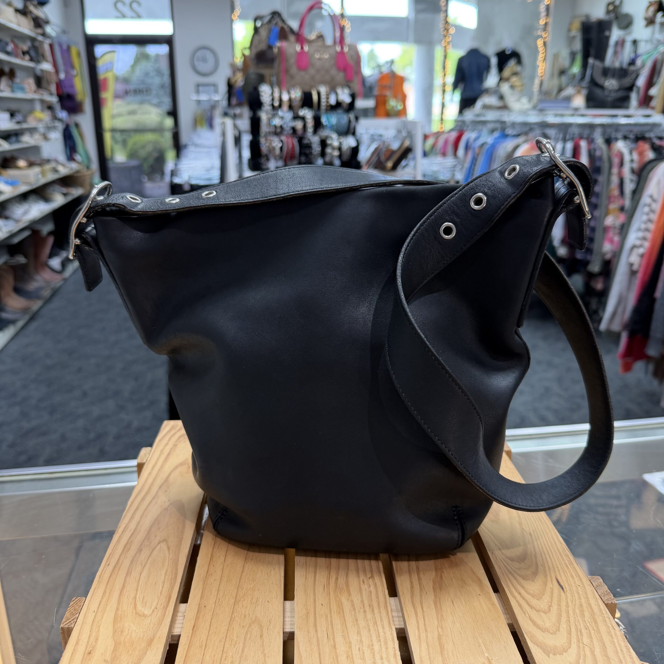Vintage Coach black leather bucket shoulder bag with adjustable strap and minimalist design displayed in a women's consignment boutique.