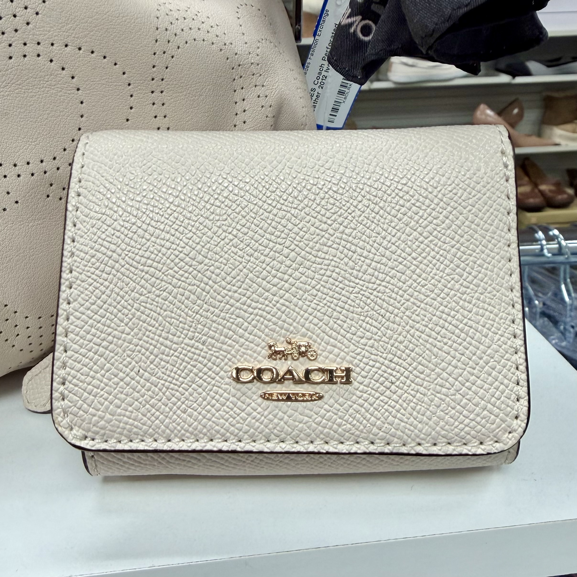 Authentic Coach light beige leather card case wallet with gold-toe Coach logo and snap closure displayed in a women's consignment boutique.